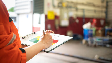 Wall Mural - a manager is holding a pen and risk matrix form with factory workshop place as blurred background. i