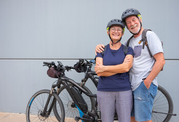 Happy and relaxed senior caucasian couple with helmet enjoying sport activity with electric bicycles in outdoors - sustainable mobility concept