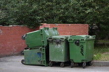 Green Plastic Dumpsters Are Stacked Against A Red Brick Wall