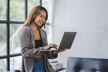 Wall Mural - Portrait of an Asian woman playing laptop at the office. Portrait of a businessman, employee, online marketing, ecommerce, online marketing concept.