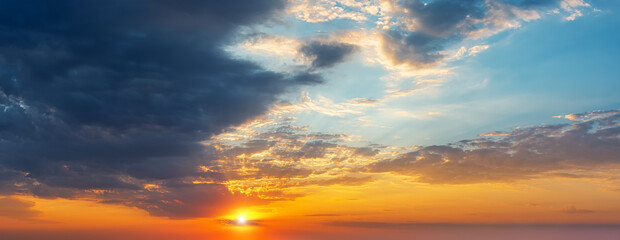 Wall Mural - setting sun in the orange blue evening sky. sun rays break through the light clouds at sunset. dark 