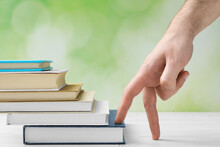Man Climbing Up Stairs Of Books With Fingers On White Wooden Table Against Blurred Background, Closeup