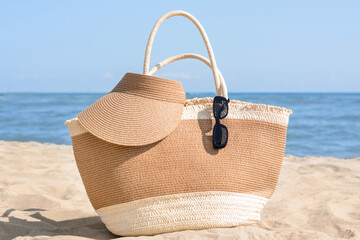 Poster - Stylish straw bag with visor cap and sunglasses on sandy beach near sea