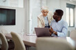 © Drazen - Senior CEO and her younger colleague talk while working on laptop in office.