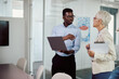 © Drazen - Young black businessman using laptop while talking to senior female executive in office.