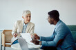© Drazen - Senior businesswoman and her young her colleague talk while going through paperwork in office.