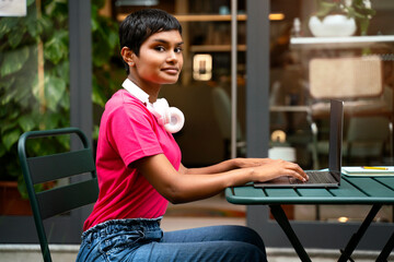 Portrait of Indian woman using laptop computer, typing, working freelance project looking at camera sitting at workplace. Successful asian student studying, online education  