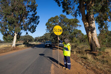 Road Traffic Controller Standing On Side Of Road With Slow-stop Lollipop Sign
