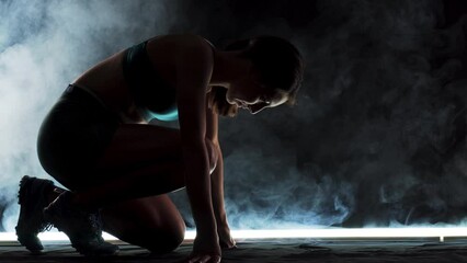 Wall Mural - Silhouette female runner in race  start position. Girl in sportswear posing on lit track with smoke in the background.