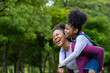 © Akarawut - African American mother is playing piggyback riding with her young daughter while having a summer picnic in the public park for wellbeing and happiness concept with copy space