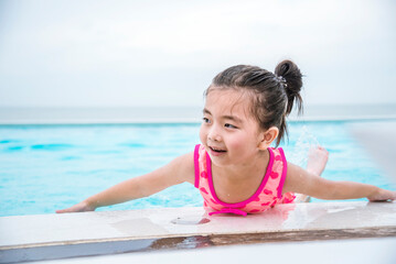 Toddler girl have fun swimming pool summer time with swimwear in blue water at hotel swimming pool outdoor. Kid swim playful water splash with happiness on summer vacation. Happy girl swim concept