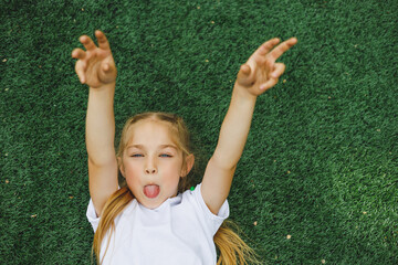 a little girl of 7-8 years old in a white t-shirt and sunglasses is sitting on the sports field. the