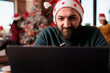 © DC Studio - Young adult working on laptop in decorated office with christmas tree and festive ornaments. Male worker using pc in workplace with xmas decorations during winter holiday season.
