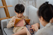 Asian boy sits on the sofa playing games with his tablet, with his single mother sitting next to him chatting with a friend on a mobile phone. A middle-aged man and woman sit in the living room