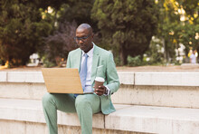 Businessman With Coffee Cup Using Laptop In Park