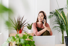 Happy woman talking on phone sitting by houseplants at home