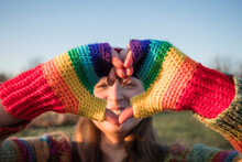 Smiling Woman With Rainbow Gloves Gesturing Heart Shape On Sunny Day