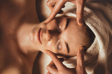 Wall Mural - top view photo of cosmetologist making facial massage treatment for patient woman face at spa salon.