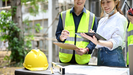 Wall Mural - Asian female architect checking some details on clipboard with a team at the construction site.