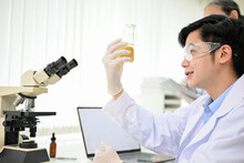 Handsome Asian Male Scientist In Gown And Goggles Holding A Erlenmeyer Flask.
