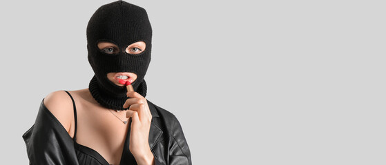 Young woman in balaclava and with lipstick on grey background with space for text