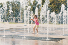 Happy Child Playing With Water Splashes In City Fountain