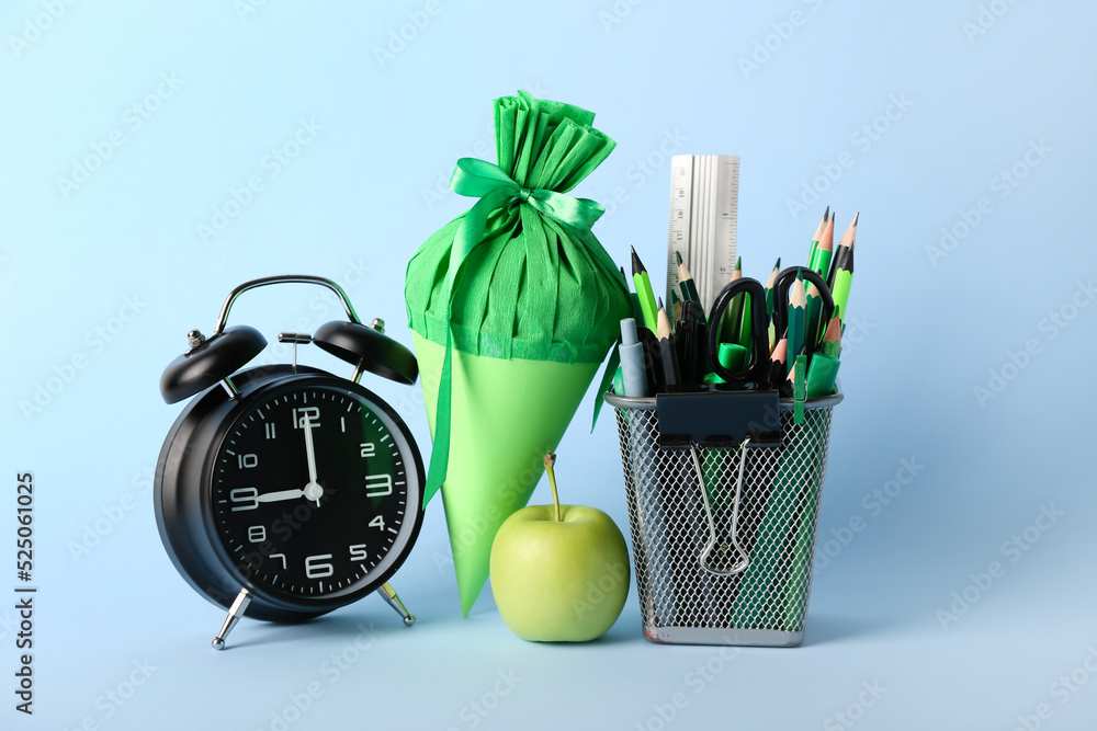 Pen cup with stationery, school cone, alarm clock and apple on blue background