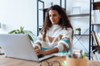 © nenetus - Concentrated beautiful business woman working with laptop while drinking coffee in living room at home.