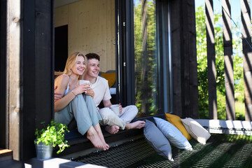 young couple sitting with cup of coffee and cuddling in terrace in their new home in tiny house in w