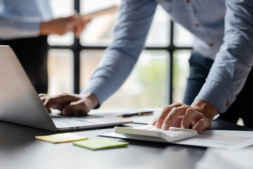 Wall Mural - Close-up of a business man using a white calculator, a financial businessman examining the numerical data on a company financial document, he uses a calculator to verify the accuracy of numbers.