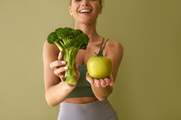 Wall Mural -  Cropped image of girl holding broccoli and green apple on green background.