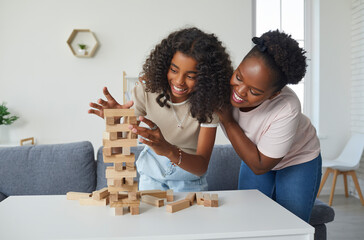 Family plays board game. Cheerful and friendly young woman and her teenage daughter are having fun playing Jenga together. Dark-skinned family spending time together at home on day off.