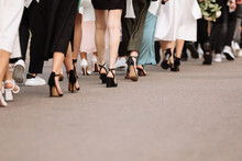 The Feet Of The Group Of People Are Walking Outdoors. Graduation Day. Stylish Young Guys And Girls In Stylish Shoes.
