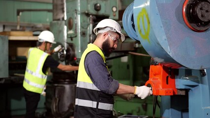 Wall Mural - Close-up portrait of latin mix race have unkempt beard and asian man worker in safety uniform, wearing helmet, glasses, vest and glove is working on heavy machinery in industrial manufacturer factory.