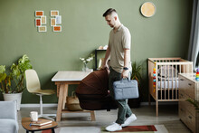 Young Dad Carrying Cradle From Pram And Bag In The Room, He Taking His Newborn Baby To Walk Outdoors