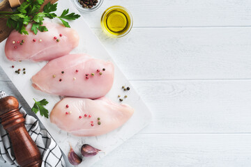 Wall Mural - Chicken breast. Two Chicken fillet with spices, olive oil and parsley on white stone cutting board on white wooden table background. Top view with copy space. Food meat cooking background.