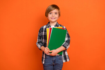 Photo of young cheerful school boy hold hands materials clever isolated over orange color background