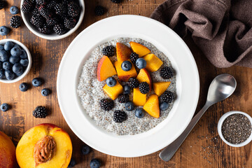 Wall Mural - Chia pudding bowl with peach and blueberries on wooden table background, top view