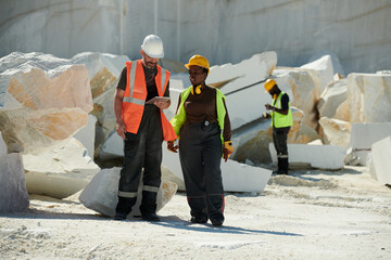 Aufkleber - Two young intercultural workers of marble quarry discussing online manual guide while standing against heaps of huge rocks