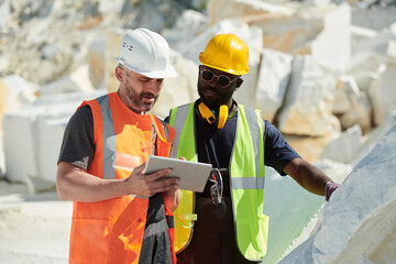 Aufkleber - Two interracial male engineers in hardhats and uniform looking at tablet screen while discussing online data or reading manual guide