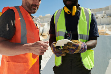 Poster - Mid section of two intercultural workers of marble quarry in uniform discussing sort of solid rock while one of them holding its part