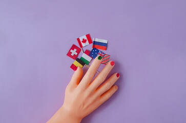 A man's hand with painted nails holding various countries flags against purple background. Creative design for LGBT or gay pride festival or celebration banner or print. Gender neutral concept.