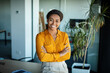 © Prostock-studio - Happy black businesswoman standing with crossed arms in front of her desk at modern office and smiling at camera