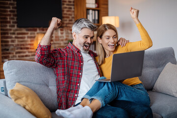 Wall Mural - Satisfied adult caucasian husband hugging wife, celebrating victory online, looking at laptop