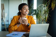 © Prostock-studio - Dreamy black businesswoman using laptop and holding coffee cup, looking aside and thinking, sitting at workplace
