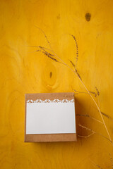 Wall Mural - Present box with blank white postcard, branch on bright yellow background, top view, copy space. Birthday, wedding, mothers, Valentines day