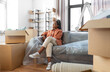 © Syda Productions - moving, people and real estate concept - happy smiling woman with boxes sitting on sofa at new home