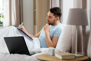 Sticker - people, technology and remote job concept - man with laptop computer and clipboard working in bed at home bedroom