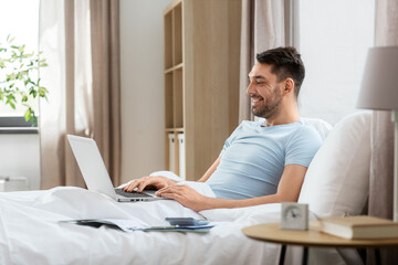 Canvas Print - people, technology and remote job concept - man with laptop computer lying in bed at home bedroom