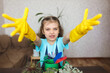 girl in blue t-shirt and yellow gloves with green watering can, paws and rake takes selfie at home